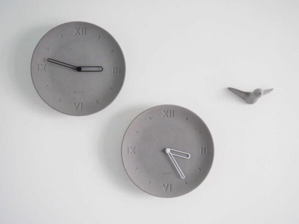 Deux horloge forme assiette béton gris clair chiffre romain aiguilles noires une blanches l'autre
