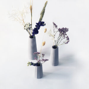 Trois petits vases béton gris clair différentes tailles surfaces facettes contentant fleurs séchées.